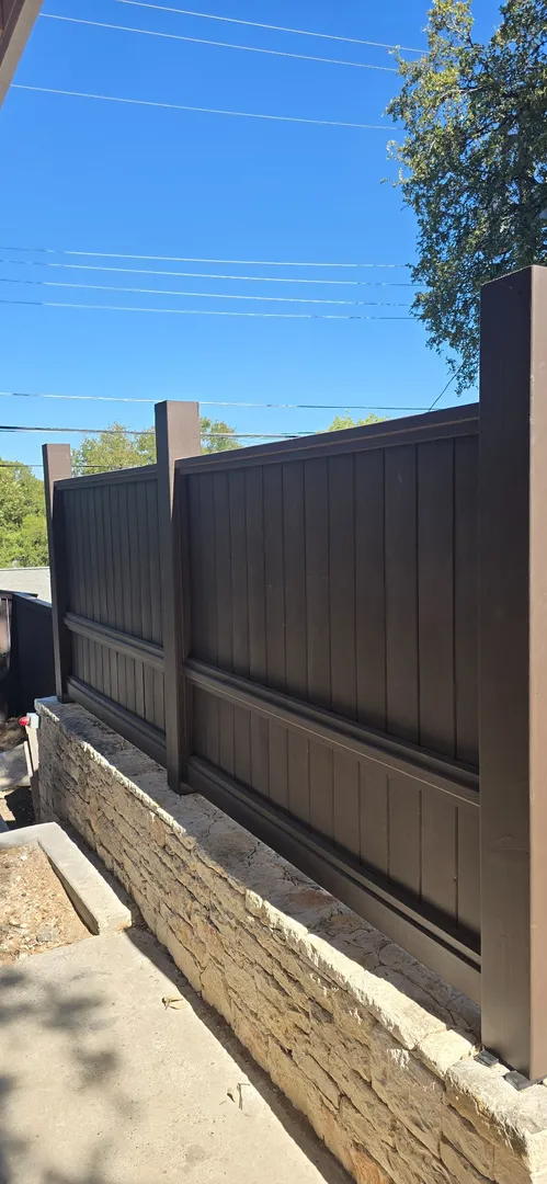 Close view of the custom dark wood privacy fence above a stone retaining wall.