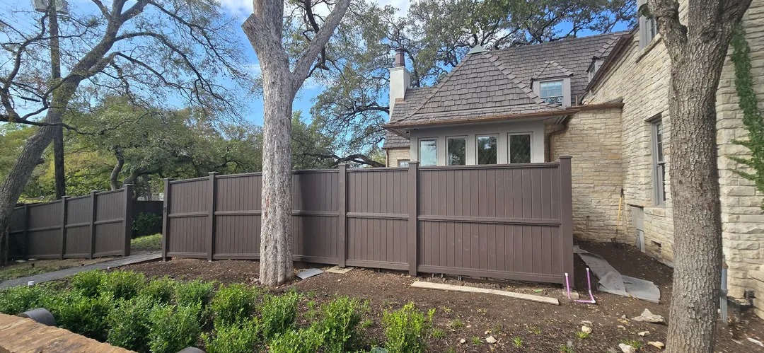 Finished dark wood privacy fence beside mature trees and landscaped grounds.