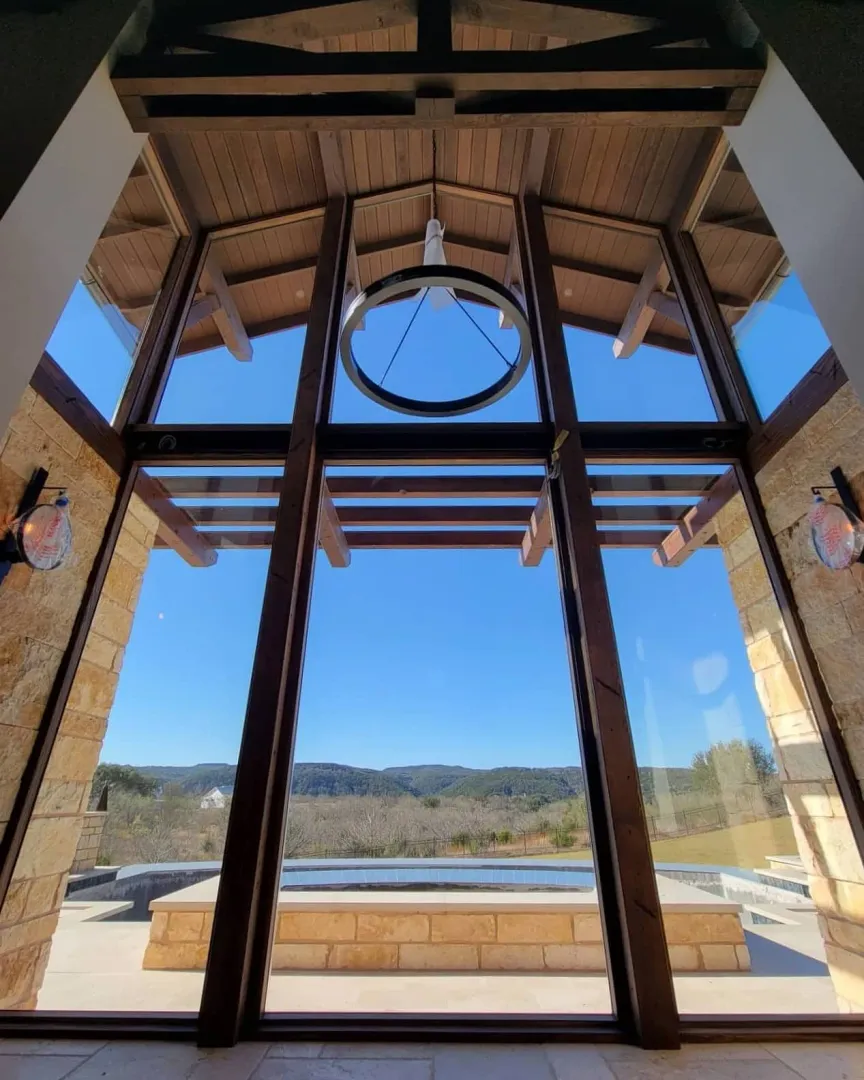 Tall glazed entry wall framed by exposed timber beams and a circular upper window.
