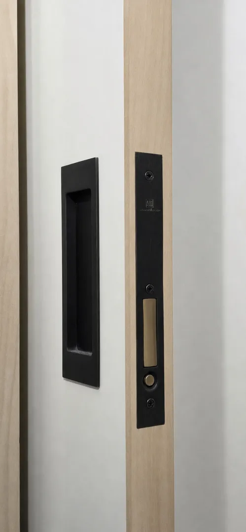 Close view of a recessed black mortise lock and strike in a wood door assembly.