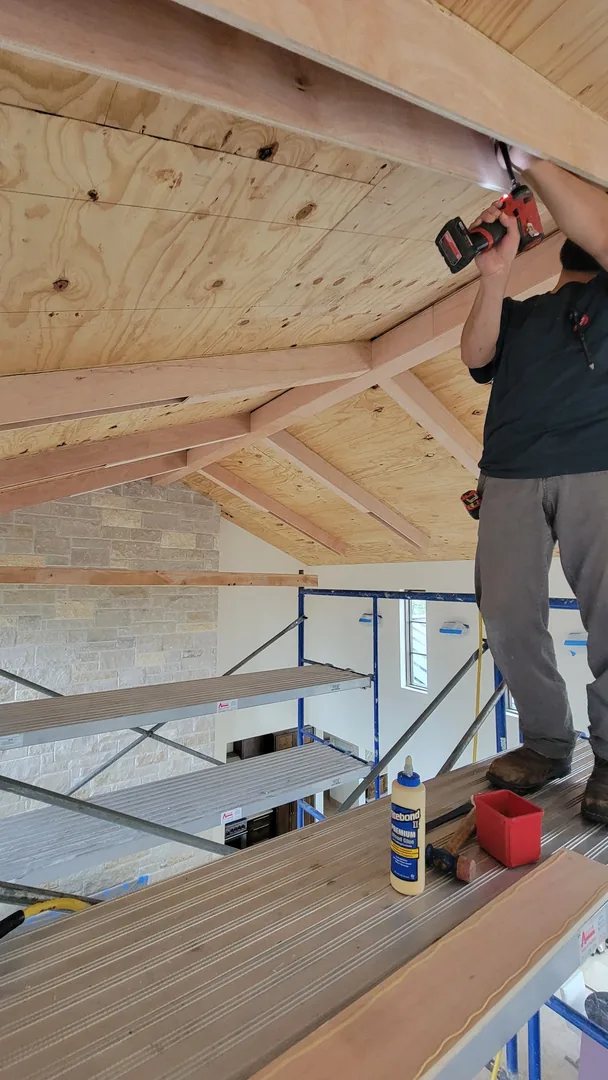 Craftsperson installing wood boards at the edge of the vaulted ceiling from a protected work platform.