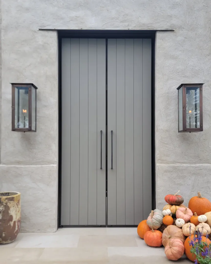 Tall custom paneled entry door closed between bronze wall lanterns.