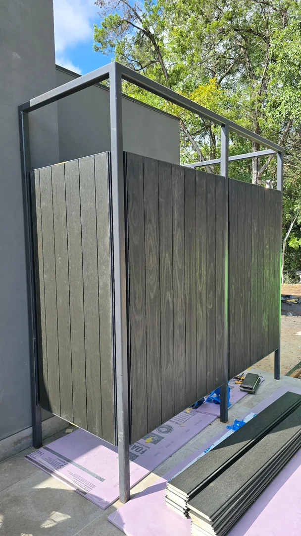 Dark vertical panels fitted into a metal-framed exterior screen beside the house during installation.