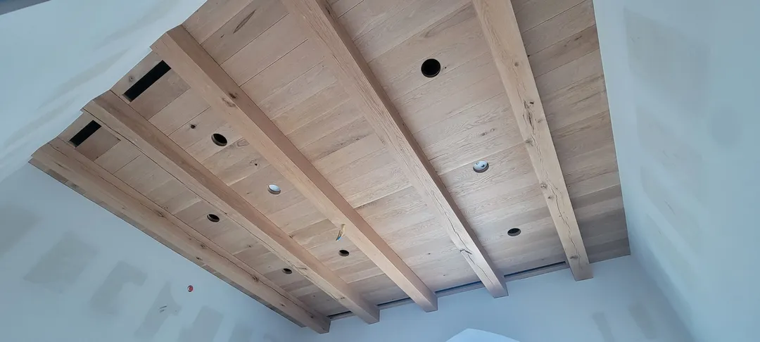 Completed wood beam-and-panel ceiling above an arched opening in a finished white room.