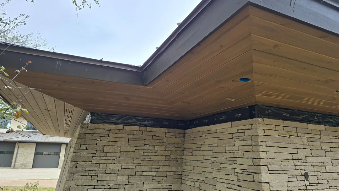 Wood soffit boards meet at an outside corner above stone walls, with vent slots and recessed light openings.