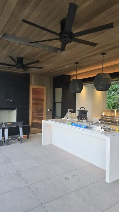 Covered outdoor kitchen with a continuous wood ceiling, black cabinetry, integrated lighting, and pendant fixtures.