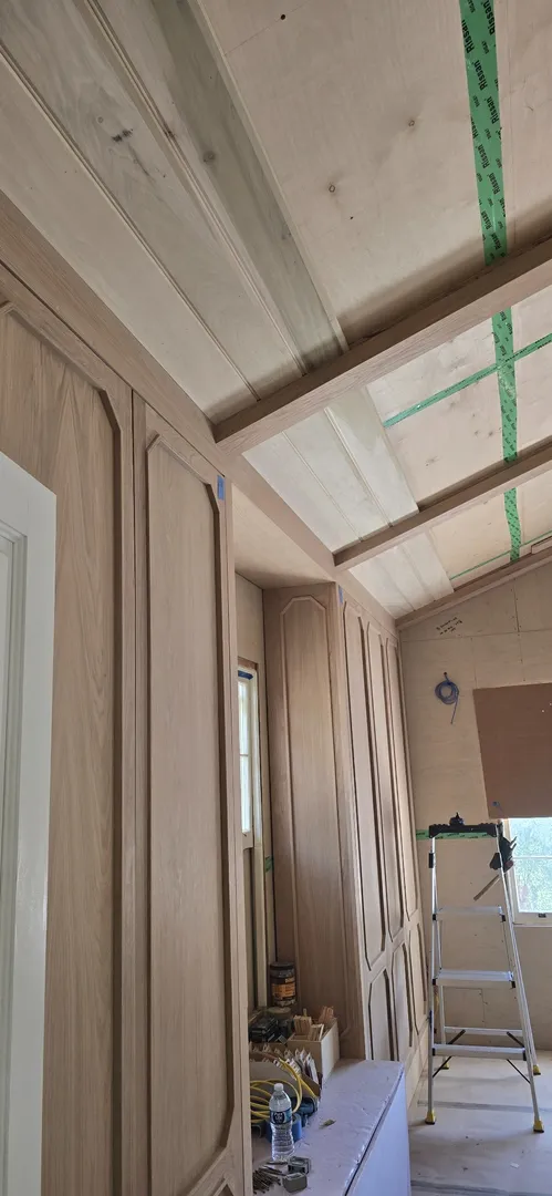 Curved white oak ceiling and wall paneling progressing around tall windows.